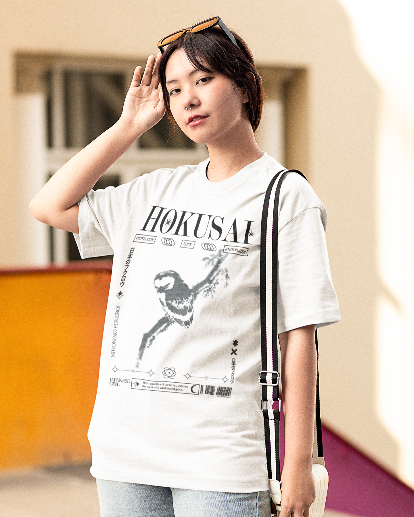 Woman wearing a white t-shirt with 'HOKUSAI' design and light blue jeans, standing outdoors.